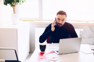 Ofiste dizüstü bilgisayar üzerinde çalışan ve telefon görüşmesi cevap genç adam