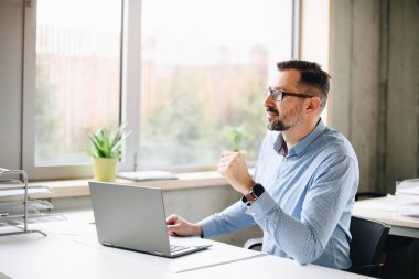 Orta Ofis dizüstü bilgisayar üzerinde çalışan tişörtlü yakışıklı adam yaşlı. Ofiste çalışan adam