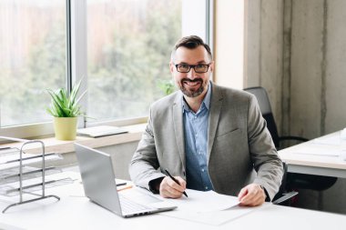 Mutlu orta yaşlı yakışıklı işadamı gömlekli ofiste dizüstü bilgisayar üzerinde çalışıyor. Ofiste çalışan adam