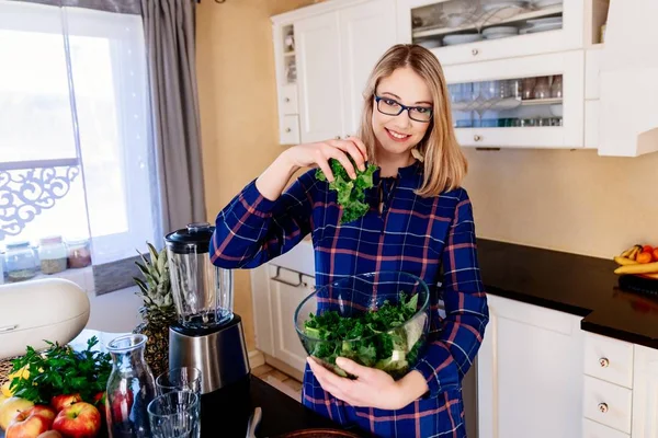 Молодая беременная женщина смешивает зеленую капусту в стеклянную миску на кухне — стоковое фото