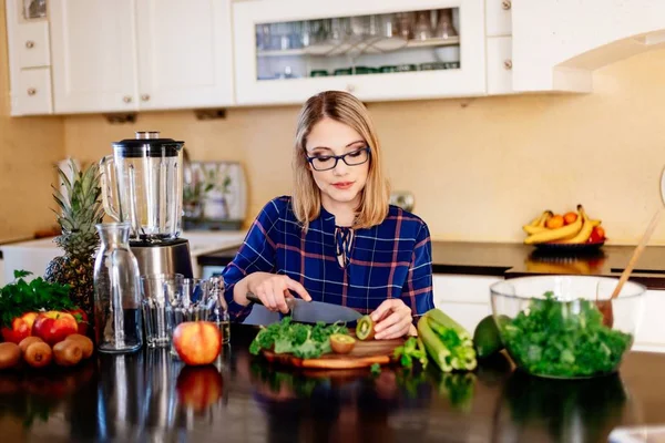 Woman cutting kiwi fruit in kitchen. — Stock Photo, Image