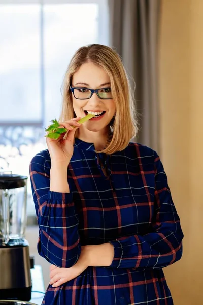 Young blonde woman eating green celery in kitchen — Stock Photo, Image