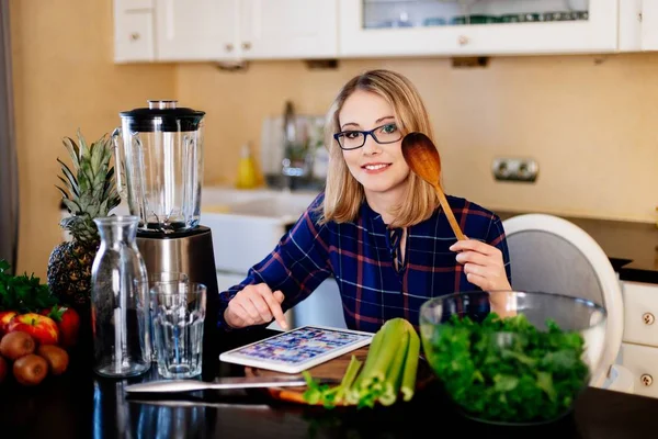 Blonde woman cooking in kitchen. Reading recipe from tablet. — Stock Photo, Image