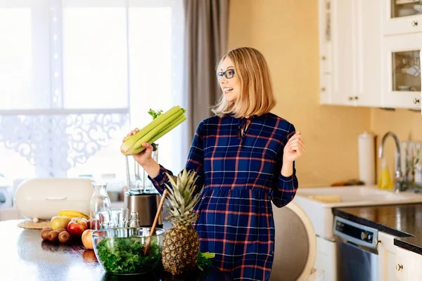 Happy young pregnant woman singing with celery in kitchen. — Stock Photo, Image