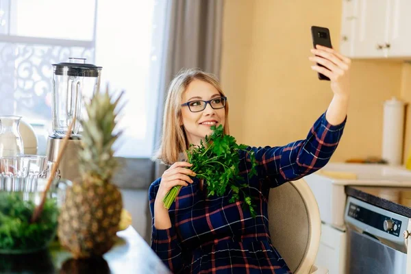 Fiatal nő élelmiszer-blogger figyelembe selfie fénykép, a petrezselymet a konyhában — Stock Fotó