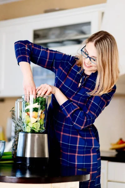 Женщина кладет фрукты и овощи в элетрический блендер . — стоковое фото