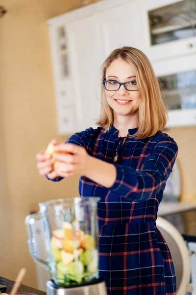 Mujer joven poniendo frutas y verduras en la licuadora eléctrica —  Fotos de Stock