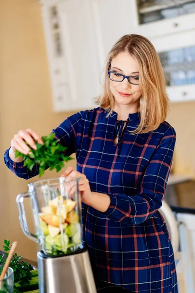 年轻女子把水果和蔬菜放入电子搅拌机 — 图库照片