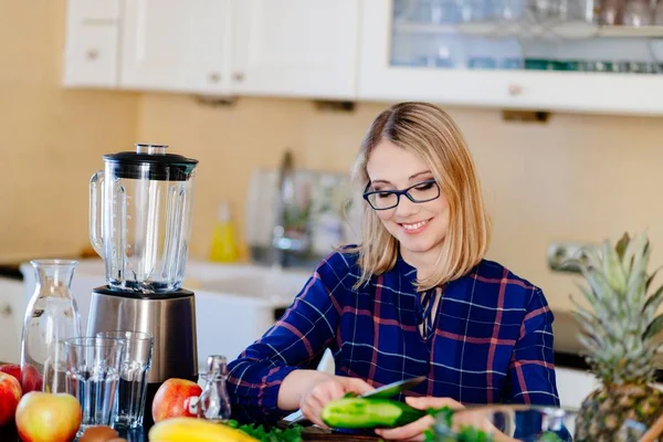 Young happy woman peeling cucumber in kitchen — Stock Photo, Image