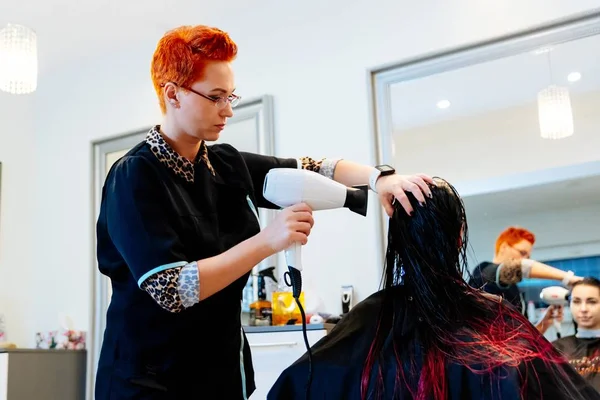 Жінка-перукар сушить молоду жінку клієнтське волосся в салоні — стокове фото