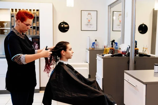 Hairdresser styling young woman customer hair in salon — Stock Photo, Image