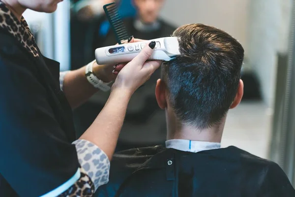 Hairdresser cutting man\'s hair with electric trimmer