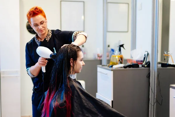 Hairdresser drying female customer hair with hand dryer in hair salon.