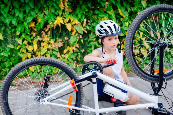 Щасливий маленький хлопчик у білому шоломі ремонтує свій велосипед — стокове фото