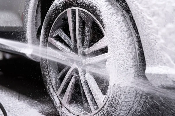 Car wash worker spraying car wheel and tire with white active cleaning foam — Stock Photo, Image