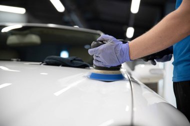 Araba yıkama stüdyosu. İşçi, çizik araba boyasını elektrikli cilasıyla parlatıyor..