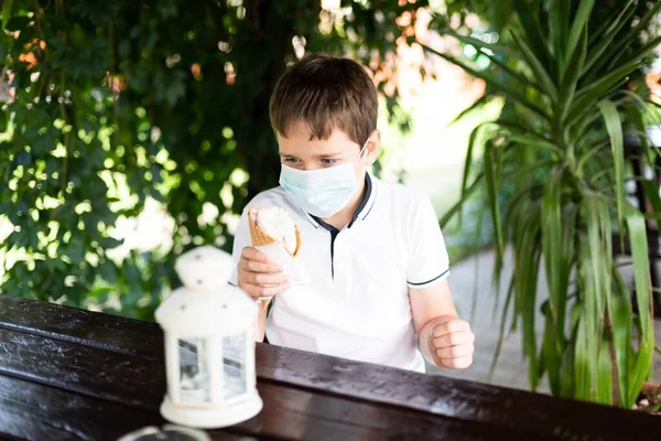 Niño tratando de comer helado. Usando máscara médica. Niño y covid-19 coronavirus — Foto de Stock