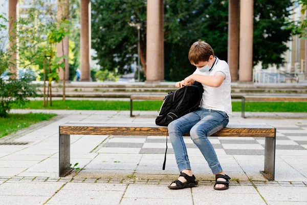 Studente in maschera medica che mette lo zaino della scuola in panchina. Scuola durante il coronavirus covid-19 pandemia — Foto Stock