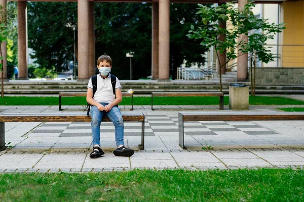 Schuljunge in medizinischer Maske sitzt auf der Bank. — Stockfoto