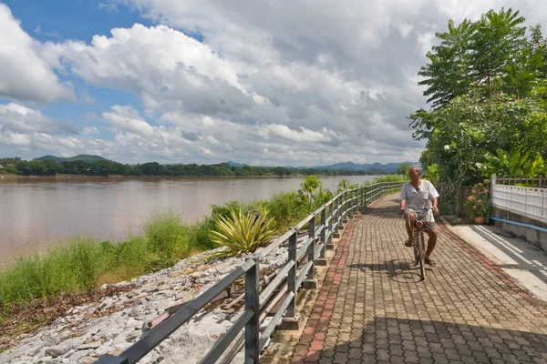 Man cycling along the Mekhong riverbank in Thailand with Laos on — Stock Photo, Image