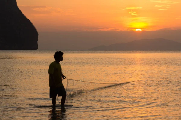 Ein Fischer zieht bei Sonnenuntergang am Strand von Rajamangala in Thailand sein Netz ein. — Stockfoto