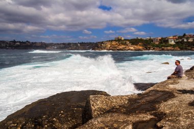 Bir adam kayalıklarda oturur dalgalı denizleri seyreder.. 
