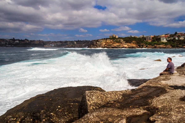  Bir adam kayalıklarda oturur dalgalı denizleri seyreder.. 