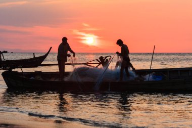 Gün batımında teknelerinde ağ sıralayan iki balıkçı, Nai Yang Sahili, Phuket, Tayland