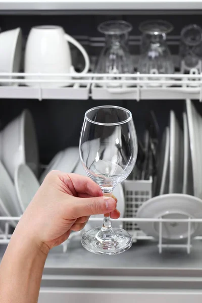 dishwasher, open and loaded with dishes, man hand taking out clean wine glass, after washing