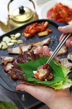 Pişmiş samgyeopsal (ızgara domuz eti barbeküsü), marul ve Kore mutfağıyla sarılmış. 