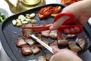 Pişmiş samgyeopsal (ızgara domuz eti barbeküsü), makas ve Kore mutfağı ile kesilir.