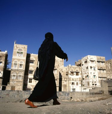 örtülü bir Müslüman kadının bir sanaa sokak, yemen.at arka plan tipik yemen evleri üzerinde yürüyor.