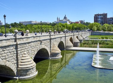 Madrid, Spain - May 15, 2018. Puente de Segovia bridge crossing the gardens of Madrid Rio at spring day with the Almudena Cathedral and the Royal Palace in background. Madrid, Spain. clipart