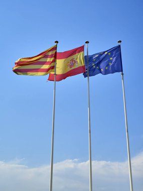 Resmi bayrakları sallayarak üzerinde mavi bir gökyüzü Catalonia, İspanya ve Avrupa Birliği (AB).