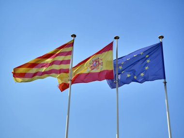 Resmi bayrakları sallayarak üzerinde mavi bir gökyüzü Catalonia, İspanya ve Avrupa Birliği (AB).