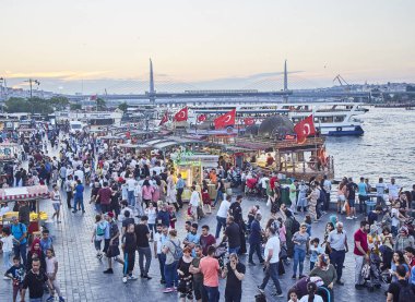 Istanbul, Türkiye - 7 Temmuz 2018. Balık Golden Horn koya bakan Eminönü İskelesi batımında, gelen turist tekneleri ve Haliç Köprüsü arka planda sandviç. Istanbul, Türkiye.