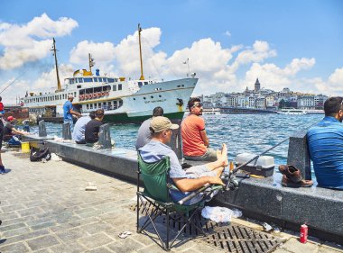 Istanbul, Türkiye - 8 Temmuz 2018. Eminönü İskelesi boğazın ağız Karaköy bölge manzarası içinde belgili tanımlık geçmiş bir görünümü ile karşı karşıya Balık tutma vatandaşlar. Istanbul, Türkiye.