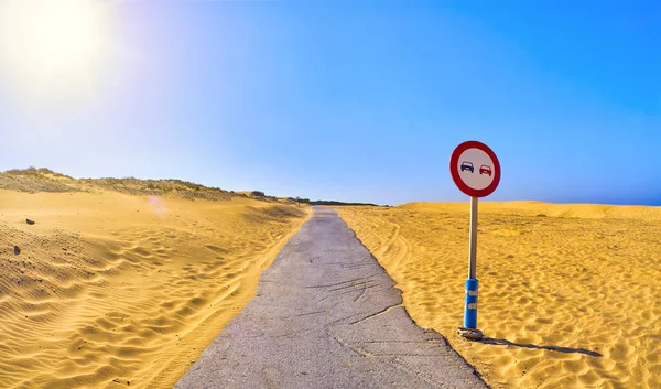 Un camino que cruza un terreno árido de dunas con una señal de no adelantamiento . —  Fotos de Stock