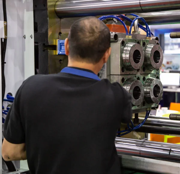 worker setting up industrial plastic injection molding press machine for manufacturing