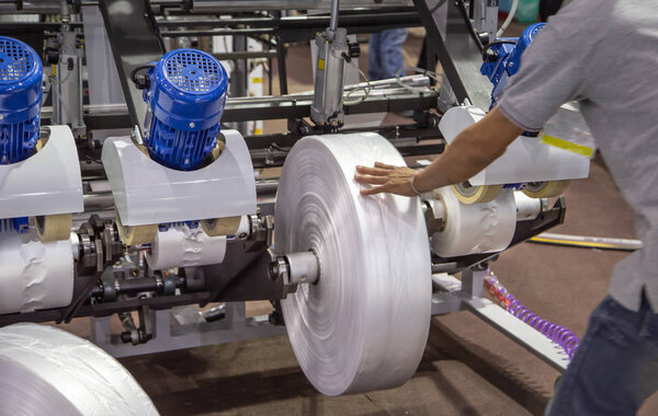 Рабочий устанавливает пленочный рулон для экструдерной машины из полиэтилена для промышленного процесса пластикового пакета
