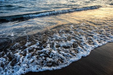 Kumlu plaj altın günbatımı sırasında yaklaşan dalgalar