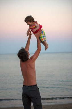 Mutlu baba ve kız birlikte denizde, yaz tatillerini üzerinde eğleniyor. Adam onun bebek kız plajda hava atma