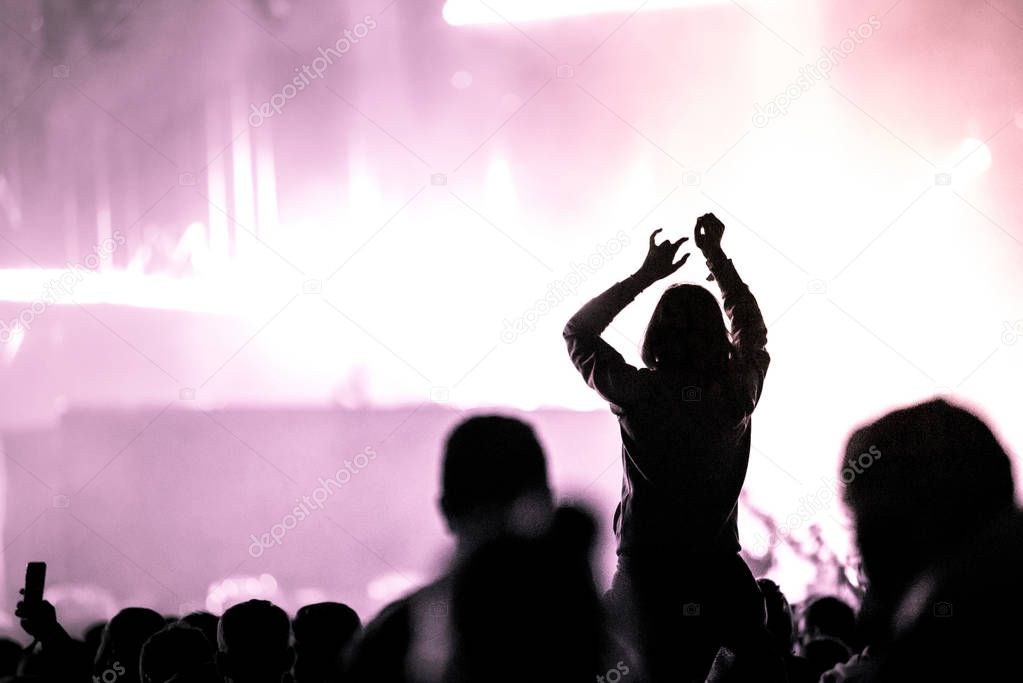 Crowd with arms outstretched at concert. Summer music festival concept. Purple stage lights
