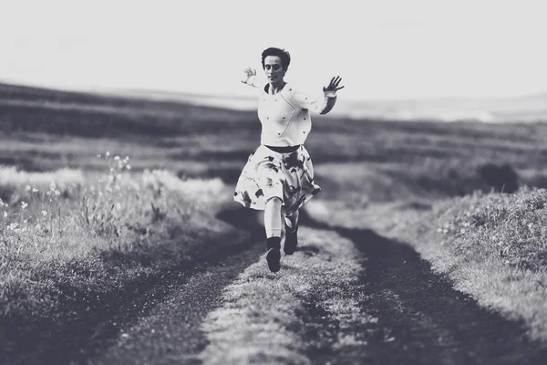 Woman in skirt running on a countryside road. Freedom concept. Black and white, toned, vintage effect