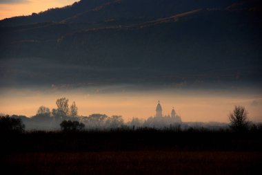 Dağ köyü puslu sabah görünümünde. Kilise kulesi üzerinde şafak pus