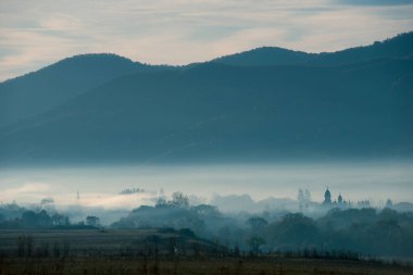 Dağ köyü puslu sabah görünümünde. Kilise kulesi üzerinde şafak pus