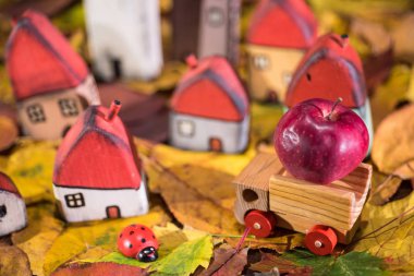 Çocuklar için oyun alanı, düzenleme boyalı oyuncak ahşap evler, bir elma taşıyan kamyon, uğur böceği üzerinde sonbahar yaprakları. Çocukluk kavramı
