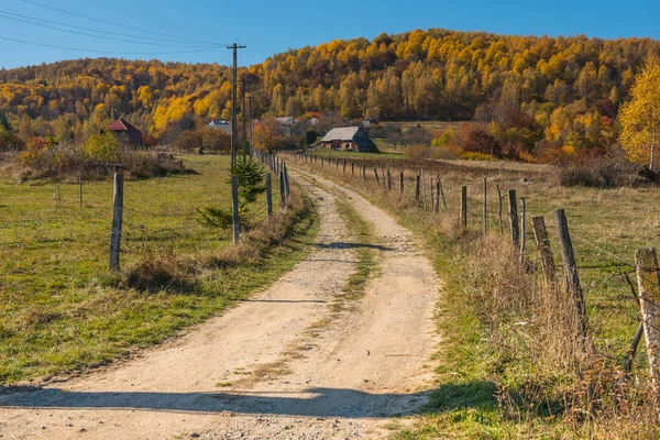 山の村を通って未舗装の道路 カラフルな秋の森と木の家 — ストック写真