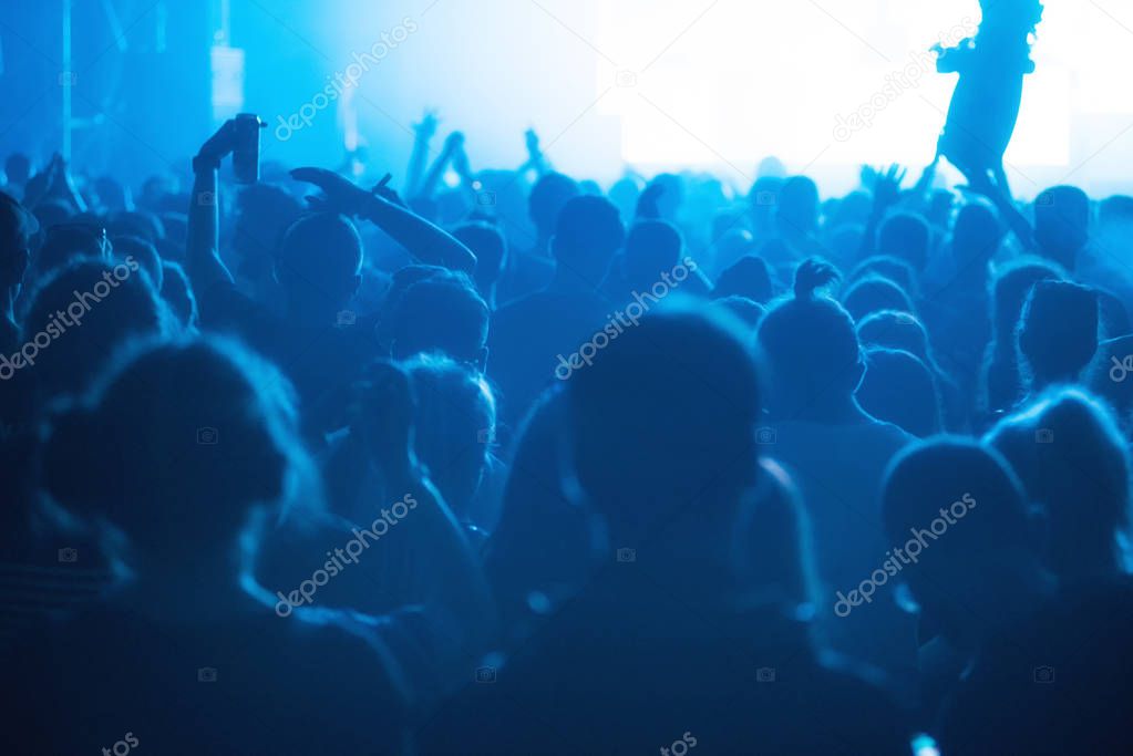 Crowd of cheerful people partying at music festival. Rear view, stage concert lights