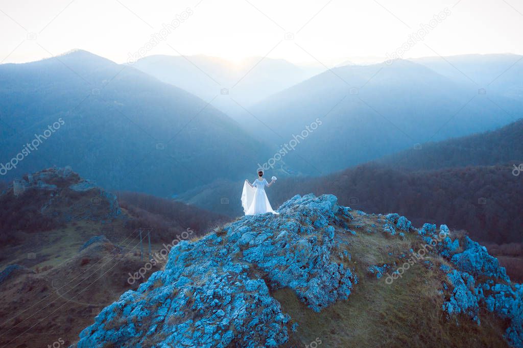 Bride in white wedding dress standing on a cliff. Aerial drone shot